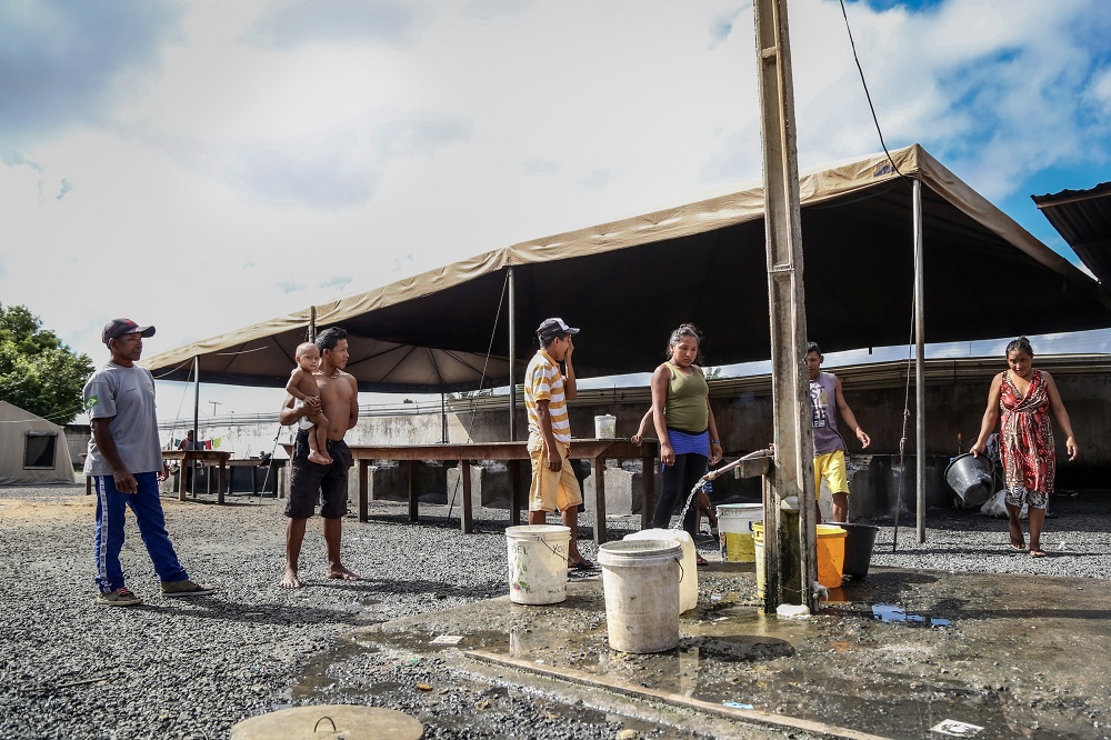 Os moradores indígenas de Pintolândia, em Boa Vista, esperam em um dos poucos lugares disponíveis para coletar água no abrigo.