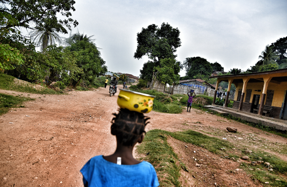 Criança leva panela com comida na cabeça, cena rotineira em Kenema, Serra Leoa