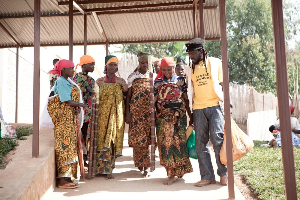 Evelyne, que está olhando diretamente para a câmera, está entre o grupo de mulheres que foram identificadas para fazer a cirurgia de reparo da fístula obstétrica na província rural de Bujumbura, no Burundi. Na foto, um promotor de saúde de MSF as acompanha ao centro Urumuri de MSF, em Gitega.