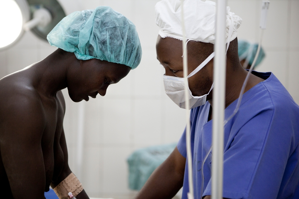 Um dos médicos tenta acalmar Evelyne. Existem centros de reparo de fístula obstétrica em algumas grandes cidades africanas, mas elas geralmente estão fora do alcance das mulheres que vivem em áreas rurais, como Gitega. Essas mulheres enfrentam a falta de cuidados obstétricos de emergência, que é a causa da maioria das fístulas.