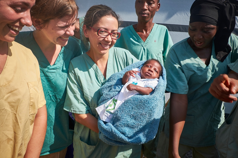 Também conhecida pelas equipes de MSF como “rainha”, Nubia leva o mesmo nome da enfermeira brasileira que lhe ofereceu cuidados em seus primeiros dias de vida. “A família me disse que a criança se chamaria Nubia, como eu. Naquele momento, tudo o que eu consegui dizer foi um simples ‘obrigada’”, relembra Nubia Aguiar, que, na foto de novembro de 2015, carrega a criança em seus braços.