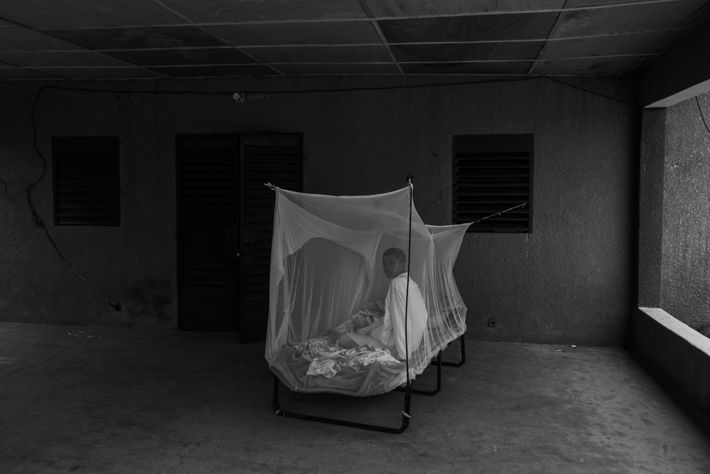Um homem se senta em uma cama sob uma rede mosquiteira, instalada para ajudá-lo a protegê-lo da malária durante a estação chuvosa. Zinder, Niger, julho de 2021.