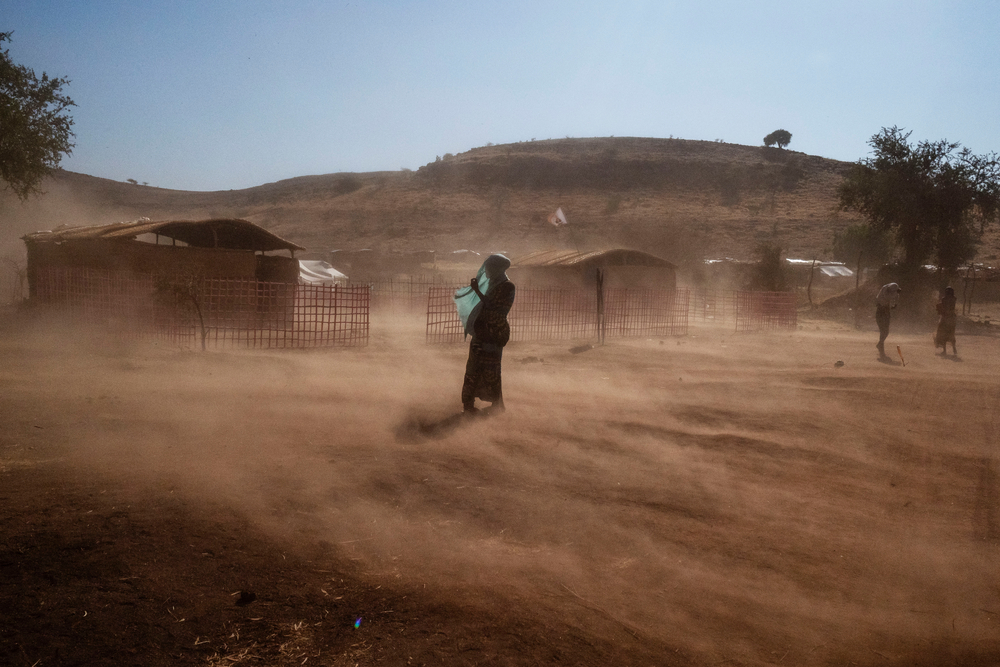Uma refugiada protege seu rosto da poeira soprada pelo vento no acampamento de refugiados de Um Rakuba, no Sudão. O povo fugiu da região Tigré do norte da Etiópia a partir de novembro de 2020 para escapar do conflito entre os militares e a Frente de Libertação do Povo de Tigré. Região de Gedaref, Sudão, dezembro de 2020.