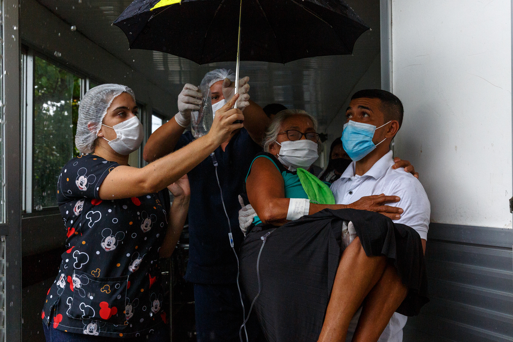 Uma paciente com COVID-19 é levada a uma ambulância, que a levará ao aeroporto para ser transferida para Manaus, capital do estado do Amazonas, para tratamento adicional. Tefé, Brasil, dezembro de 2020.