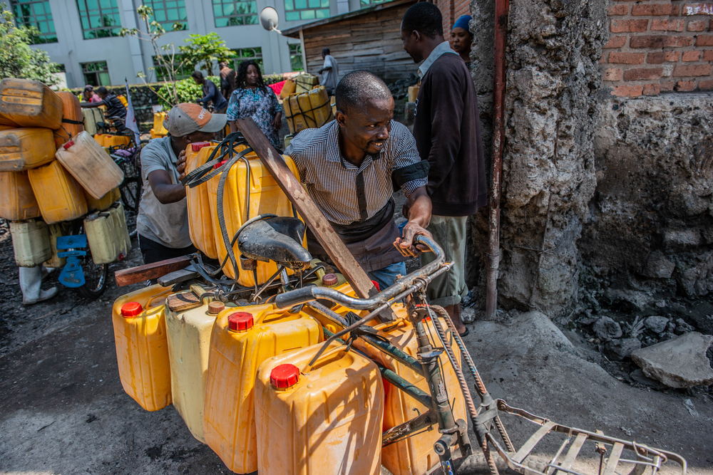 Jean-Claude empurra sua bicicleta cheia de galões de água; a necessidade de água potável tornou-se crítica após a erupção do vulcão Nyiragongo, em 22 de maio. Goma, República Democrática do Congo, junho de 2021.