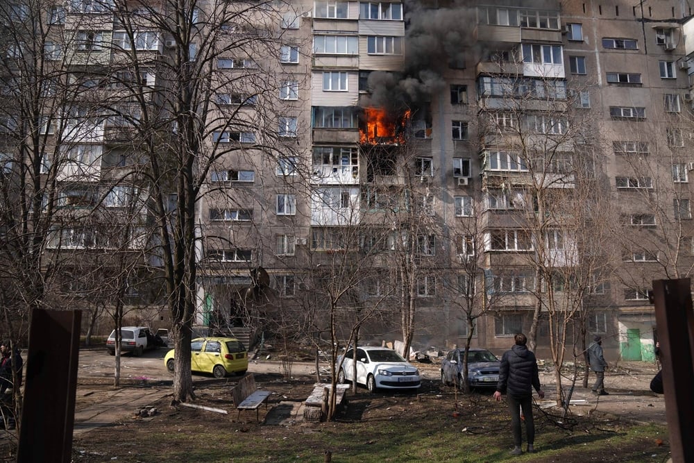 Pessoas olham para um prédio em chamas depois de um bombardeio em Mariupol, após a escalada da guerra na Ucrânia, no final de fevereiro. Foto: Evgeniy Maloletka/AP Photo, Ucrânia, março de 2022.