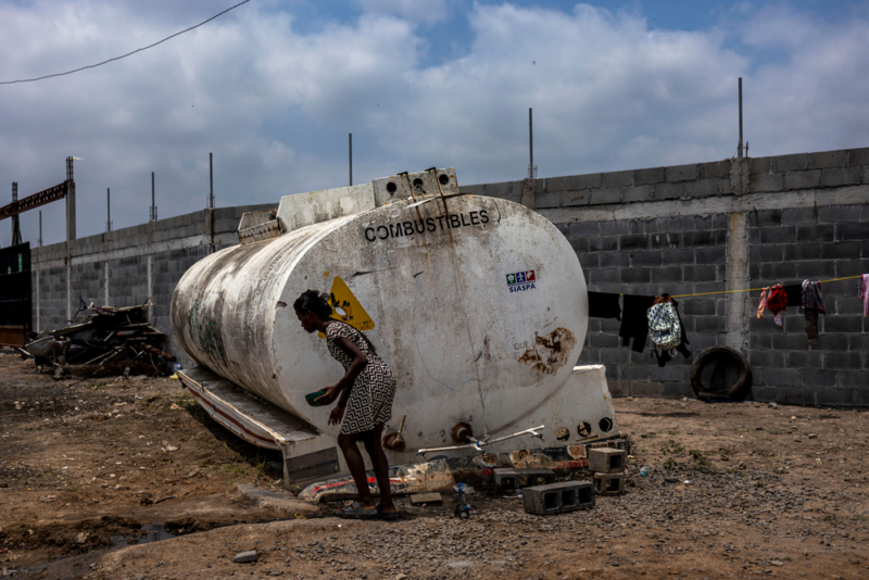 Uma mulher haitiana extrai água de um antigo caminhão-pipa que agora está sendo usado como tanque de água no canteiro de obras do futuro abrigo para migrantes. Foto: Yael Martínez/Magnum, Reynosa, México, maio de 2022.