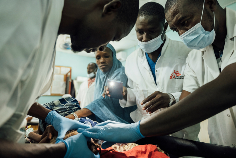 Halima Hamadou está sendo consolada por sua mãe, Zeinaolou Hamadou, enquanto uma equipe médica de MSF trata seu ferimento na cabeça. Foto: Oliver Barth/MSF, Níger, junho de 2022.