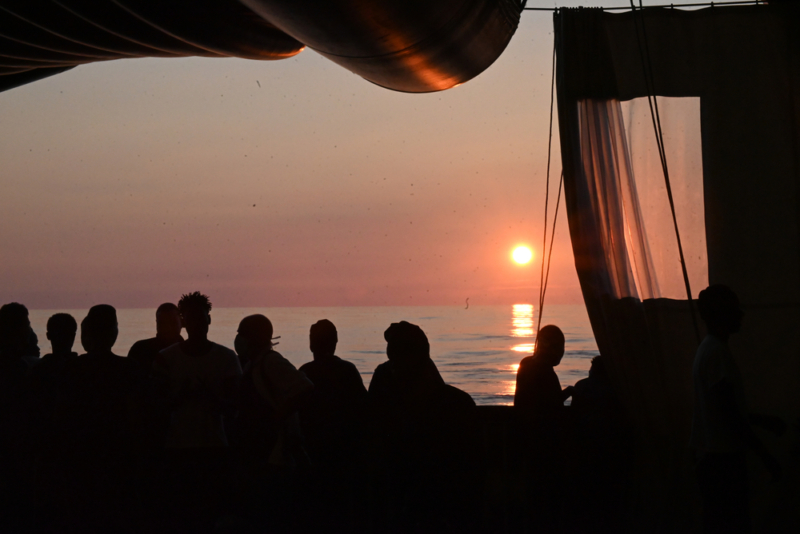 O sol se põe no horizonte enquanto os sobreviventes resgatados no Mar Mediterrâneo esperam por um lugar seguro para desembarcar. Foto: Candida Lobes/MSF, Mar Mediterrâneo Central, outubro de 2022.