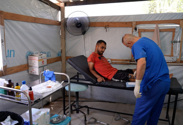 Profissional de MSF examina o ferimento de Saad Hussein, que  vive com um fixador externo após ter sido ferido em 2025 durante uma distribuição de alimentos realizada pela Fundação Humanitária de Gaza. Centro de Atenção Primária à Saúde Al Mawasi, Khan Younis, Gaza. ©Nour Alsaqqa/MSF