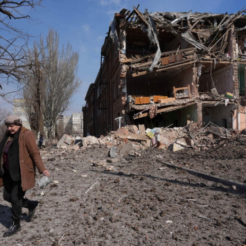 Uma mulher caminha perto de um prédio destruído por um bombardeio em Mariupol. Ucrânia, 13 de março de 2022. | Foto: Evgeniy Maloletka/AP Photo