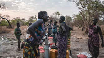 Sera James, moradora da comunidade de Akello, no Sudão do Sul, retira água do poço enquanto conversa com suas amigas. ©Njiiri Karago/MSF