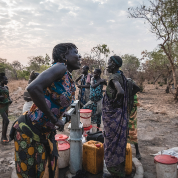 Sera James, moradora da comunidade de Akello, no Sudão do Sul, retira água do poço enquanto conversa com suas amigas. ©Njiiri Karago/MSF
