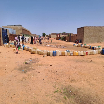 Em El Geneina, as pessoas organizam seus galões de água vazios e esperam à distância sua vez de abastecer. Elas evitam ficar paradas em grupos porque podem se tornar alvos de violência. Foto: MSF