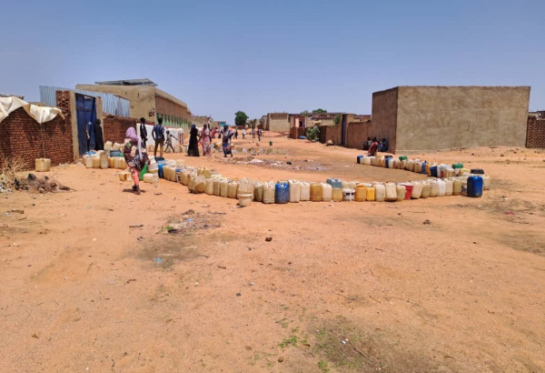 Em El Geneina, as pessoas organizam seus galões de água vazios e esperam à distância sua vez de abastecer. Elas evitam ficar paradas em grupos porque podem se tornar alvos de violência. Foto: MSF