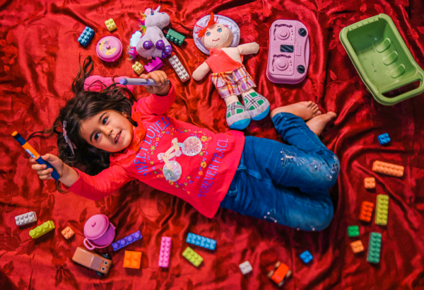 Siwar segura sua caneta de insulina, deitada entre seus brinquedos, na casa improvisada de sua família em Arsal. Ela foi diagnosticada com diabetes tipo 1 e frequenta a clínica de MSF na cidade para tratamento. © Carmen Yahchouchi/MSF, Líbano, maio de 2023