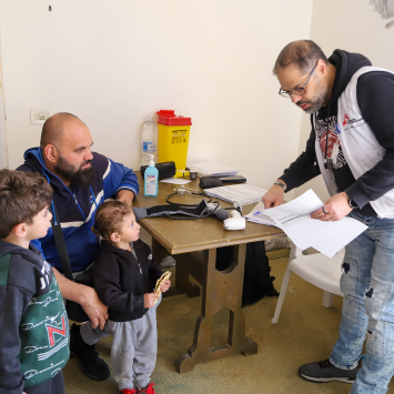 Ali e Elias acompanham o pai em uma consulta na unidade médica móvel de MSF em Al Merouaniye. Os dois irmãos estão entre as muitas crianças que se abrigam com suas famílias no Hotel Montana. © Maryam Srour/MSF