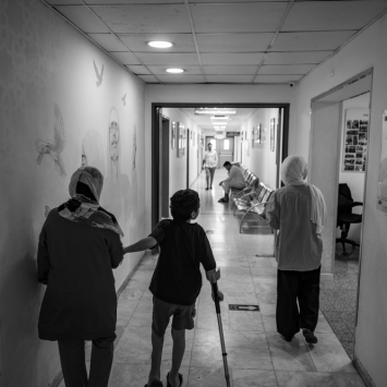 Hazem, de 8 anos (ao centro), caminha ao lado de sua mãe, Eman (à esquerda), e sua irmã, Deema (à direita), no corredor do hospital de cirurgia reconstrutiva de MSF em Amã, Jordânia, em 27 de agosto de 2024. Eles foram evacuados de Gaza. ©Moises Saman
