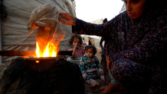 Sem acesso a gás de cozinha, Yasmin, deslocada pela guerra em Gaza, precisa acender uma fogueira usando plástico para preparar uma refeição para os seus filhos. © Ibrahim Nofal