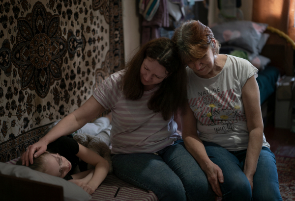 Polina (à esquerda), ao lado de sua mãe, Hanna Bila (centro), e sua avó, Tetiana Yakishina (à direita), no quarto que compartilham no centro de pessoas deslocadas internamente em Vinnytsia, na Ucrânia. © Caroline Thirion/MSF