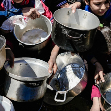 Crianças palestinas seguram panelas vazias em uma cozinha comunitária. Norte de Gaza, fevereiro de 2025. ©Nour Alsaqqa/MSF