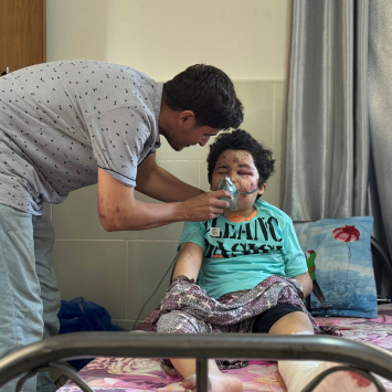 Kareem, 8 anos, é amparado pelo pai, Ahmed, cirurgião de MSF, após ser ferido em um ataque aéreo à sua casa na cidade de Gaza, em 27/06. @ Nour Alsaqqa/MSF