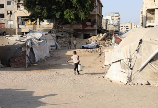 Menino palestino carrega um galão d'água até a tenda onde mora sua família, deslocada pela guerra. Gaza, agosto de 2025. ©Nour Alsaqqa/MSF