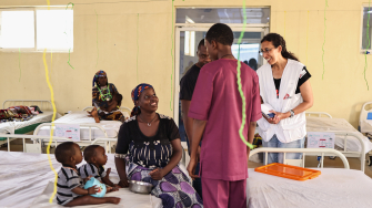 Katrin Kisswani (com o uniforme de MSF, à direita) conversa com Binta Abdulraziqu, mãe de gêmeos de 12 meses que estão em tratamento contra a desnutrição no Centro de Nutrição Terapêutica de MSF. ©Abba Adamu Musa/MSF