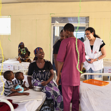 Katrin Kisswani (com o uniforme de MSF, à direita) conversa com Binta Abdulraziqu, mãe de gêmeos de 12 meses que estão em tratamento contra a desnutrição no Centro de Nutrição Terapêutica de MSF. ©Abba Adamu Musa/MSF