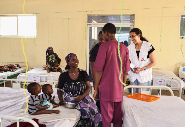 Katrin Kisswani (com o uniforme de MSF, à direita) conversa com Binta Abdulraziqu, mãe de gêmeos de 12 meses que estão em tratamento contra a desnutrição no Centro de Nutrição Terapêutica de MSF. ©Abba Adamu Musa/MSF
