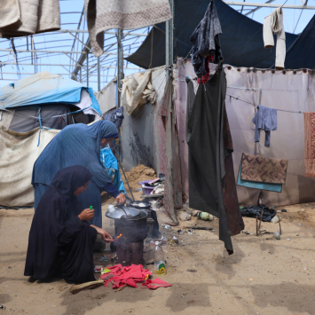 Mãe e filha deslocadas pela guerra em Gaza preparam uma refeição com métodos improvisados e inseguros em uma tenda em Mawasi, Khan Younis. ©Motasem Abu Aser/MSF