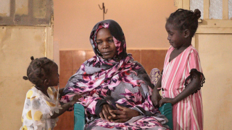 Uma mãe com suas filhas em uma unidade de saúde apoiada por MSF em Tawila, Sudão. Após mais de dois anos de dificuldades e deslocamentos sucessivos, ela relata alívio por finalmente ter acesso a cuidados médicos para si e sua família. Sudão. 2024. ©Mohammed Jamal Jibreel