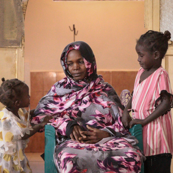 Uma mãe com suas filhas em uma unidade de saúde apoiada por MSF em Tawila, Sudão. Após mais de dois anos de dificuldades e deslocamentos sucessivos, ela relata alívio por finalmente ter acesso a cuidados médicos para si e sua família. Sudão. 2024. ©Mohammed Jamal Jibreel