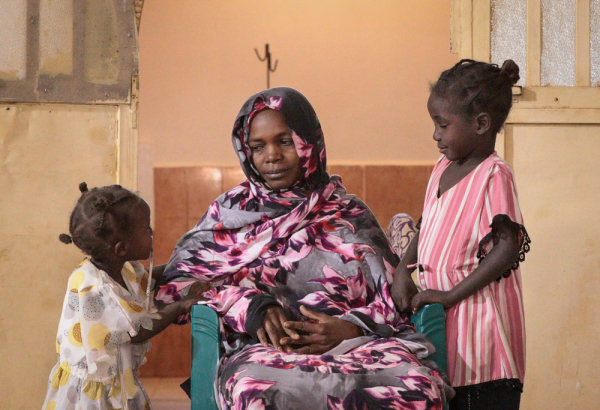 Uma mãe com suas filhas em uma unidade de saúde apoiada por MSF em Tawila, Sudão. Após mais de dois anos de dificuldades e deslocamentos sucessivos, ela relata alívio por finalmente ter acesso a cuidados médicos para si e sua família. Sudão. 2024. ©Mohammed Jamal Jibreel